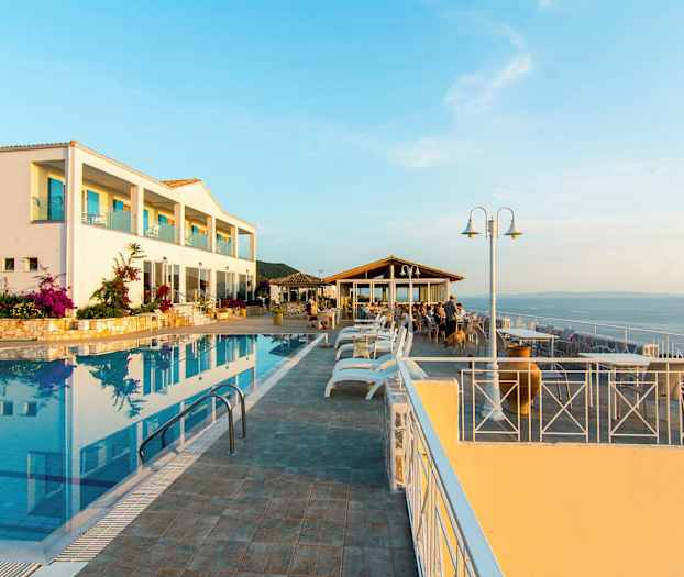 En hotellbygning ved et utendørs basseng og en sittegruppe med utsikt over havet. (AI-generert tekst)