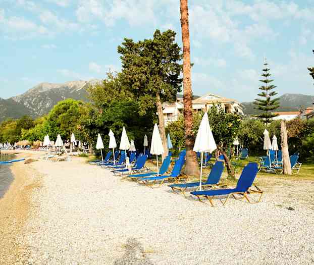 En strand med solsenger og parasoller, omgitt av grøntområder og bygninger i bakgrunnen. (AI-generert tekst)