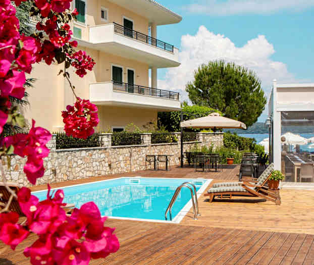 Bilde av en bygning med balkonger, et basseng og møbler på en solterrasse med blomster i forgrunnen. (AI-generert tekst)