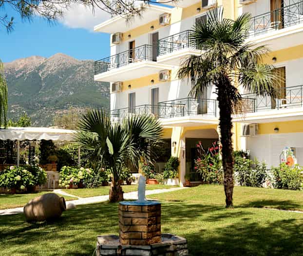 Hotellhagen med grøntområder, en fontene og bygningen i bakgrunnen. (AI-generert tekst)