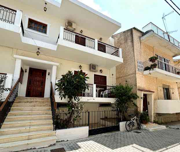 En bygning med flere etasjer, balkonger og en hage foran en steinlagt gate. (AI-generert tekst)