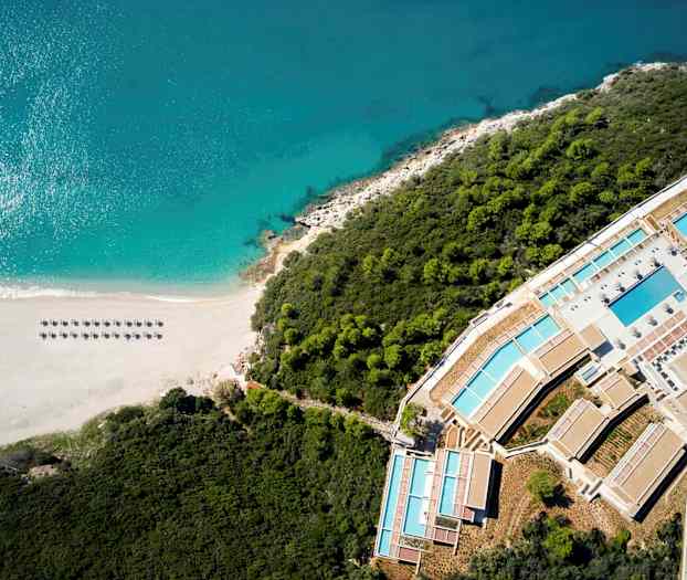 Luftfoto av en strand ved havet, omgitt av skog og et feriested. (AI-generert tekst)