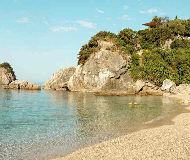 En strand med klart vann og klipper i bakgrunnen. (AI-generert tekst)