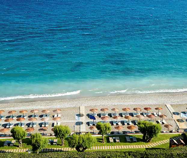 Utsikt over en strand med parasoller og solsenger mot et blått hav. (AI-generert tekst)