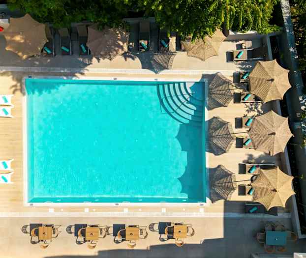 Bilde av et utendørs svømmebasseng omgitt av solsenger med parasoller og bord med stoler. (AI-generert tekst)