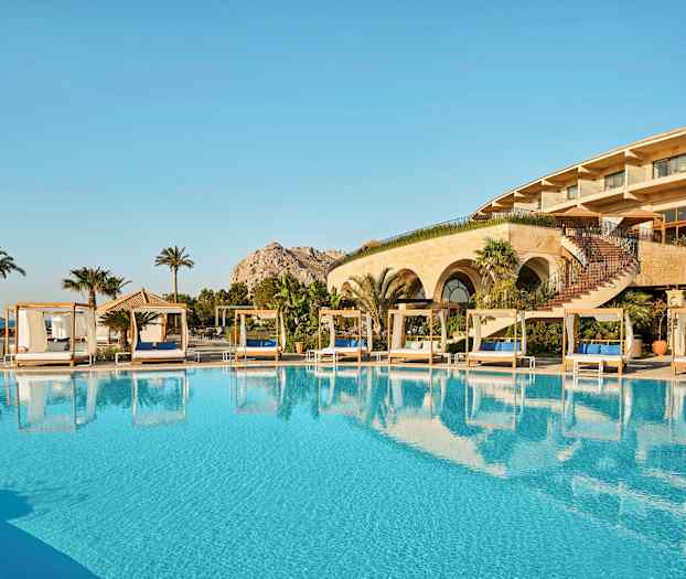 Et utendørs basseng med solsenger og et hotell i bakgrunnen. (AI-generert tekst)