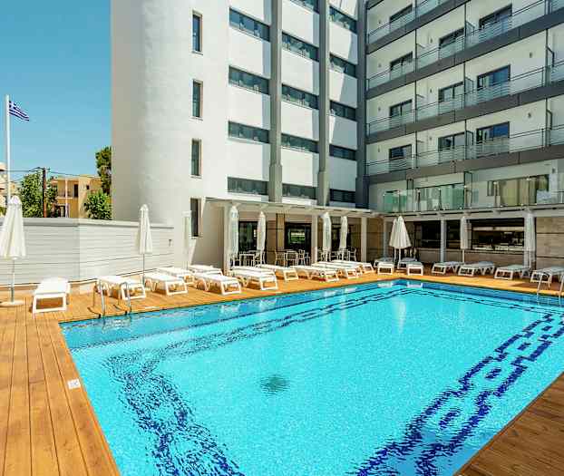 Hotellbasseng med solsenger og parasoller, omgitt av bygninger. (AI-generert tekst)