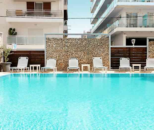 Basseng med solsenger og bord foran bygninger. (AI-generert tekst)