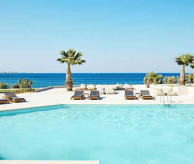 Bassengområde ved sjøen med solsenger og palmer. (AI-generert tekst)