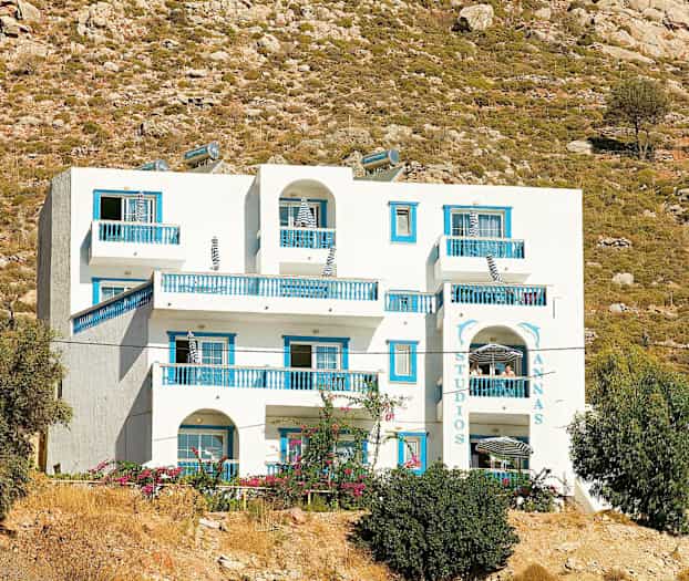 Hvit bygning med blå detaljer mot en bakgrunn av røft landskap. (AI-generert tekst)