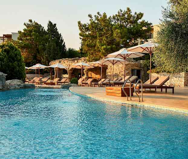 Utendørsbasseng med solsenger og parasoller ved siden av under skyggefulle trær. (AI-generert tekst)