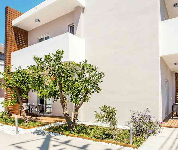 Hvit bygning med tredetaljer, en terrasse og frodig hage. (AI-generert tekst)