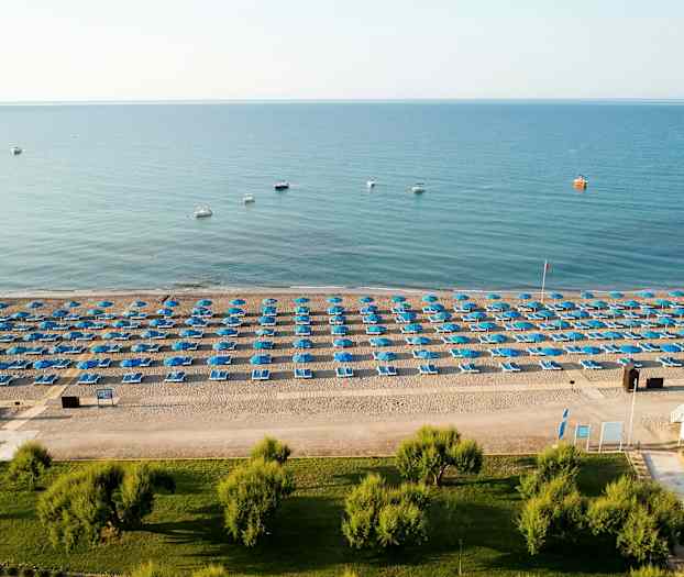 En strand med blå parasoller og solsenger ordnet i rekker. (AI-generert tekst)