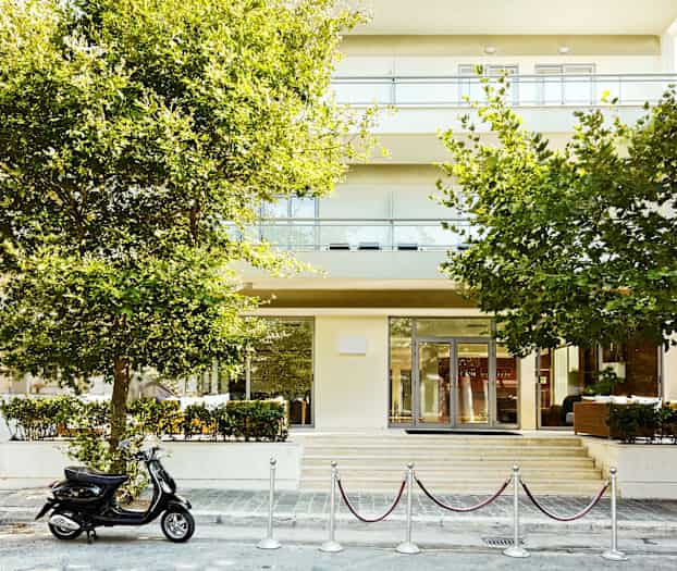 En bygning med trær i forgrunnen og en parkert scooter foran inngangen. (AI-generert tekst)
