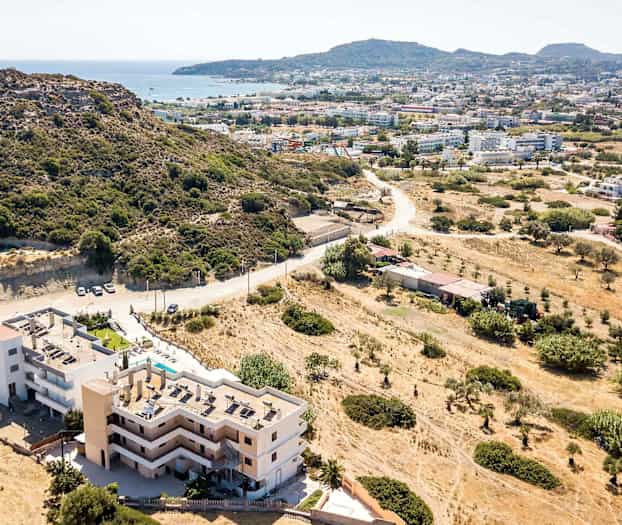 Luftfoto av en bygning nær en fjellskråning med utsikt over en by og sjøen. (AI-generert tekst)