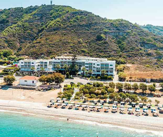 Strand med solsenger og parasoller, bak ligger en bygning ved en fjellside. (AI-generert tekst)