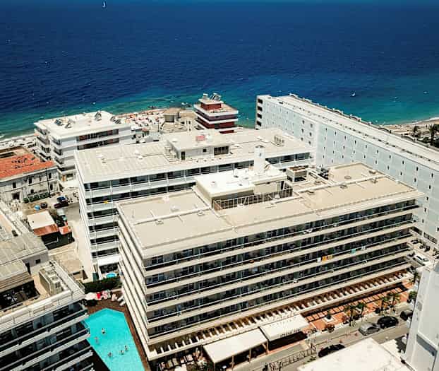 Flyfoto av hoteller og en strand ved sjøen. (AI-generert tekst)