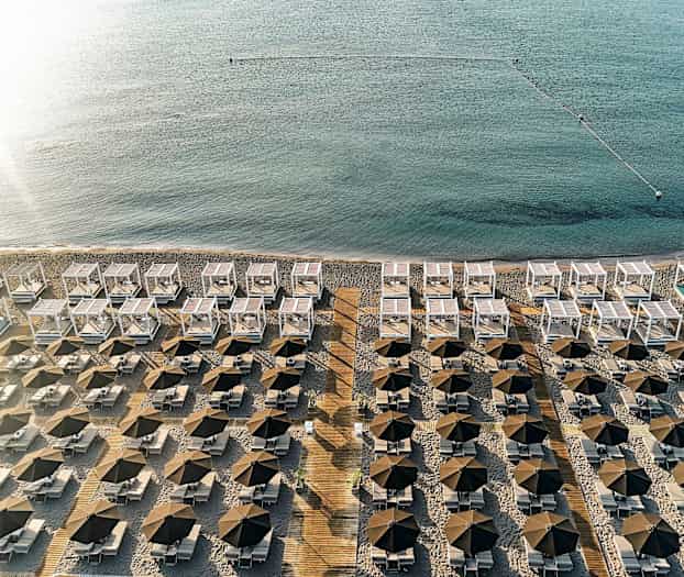 En utsikt over en strand med rader av parasoller, solsenger og hvite solskjermer nær sjøen. (AI-generert tekst)