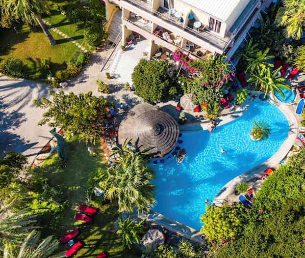 Utsikt ovenfra over et bassengområde omgitt av grønne vekster og et hotell. (AI-generert tekst)