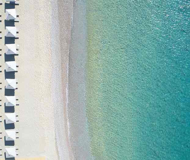 Luftfoto av strand med parasoller og klart turkis vann. (AI-generert tekst)