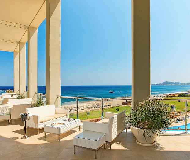 Utsikt over en terrasse med sitteplasser, mot stranden og havet. (AI-generert tekst)