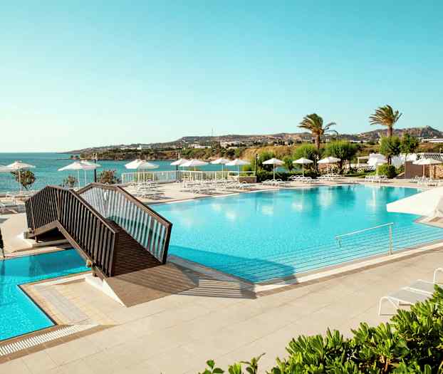 Stor basseng med solsenger og parasoller, utsikt mot sjøen og vegetasjon. (AI-generert tekst)