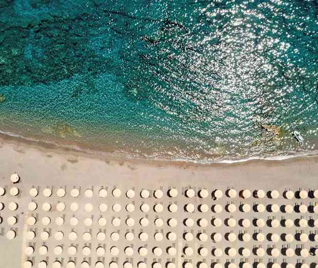 Strand med parasoller sett ovenfra nær klart vann. (AI-generert tekst)