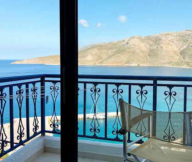 Utsikt fra en balkong med en stolrygg i forgrunnen, mot sjøen og fjell i det fjerne. (AI-generert tekst)