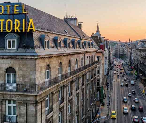 Utsikt over en bygning med teksten "HOTEL ASTORIA" og en travel gate i bymiljø under en solnedgang. (AI-generert tekst)