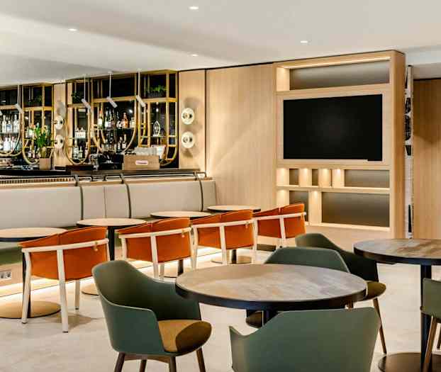 En hotellbar med sitteplasser og bord, omgitt av en moderne og lys interiørdesign. (AI-generert tekst)