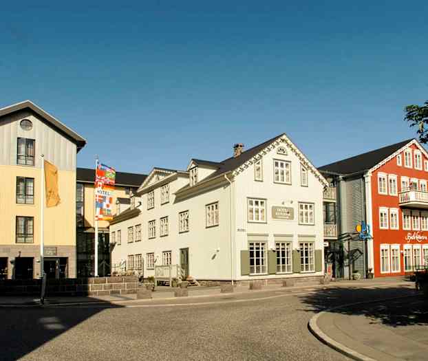 Bilde av fargerike bygninger med hotell og restaurant nær en gate med fortau. (AI-generert tekst)