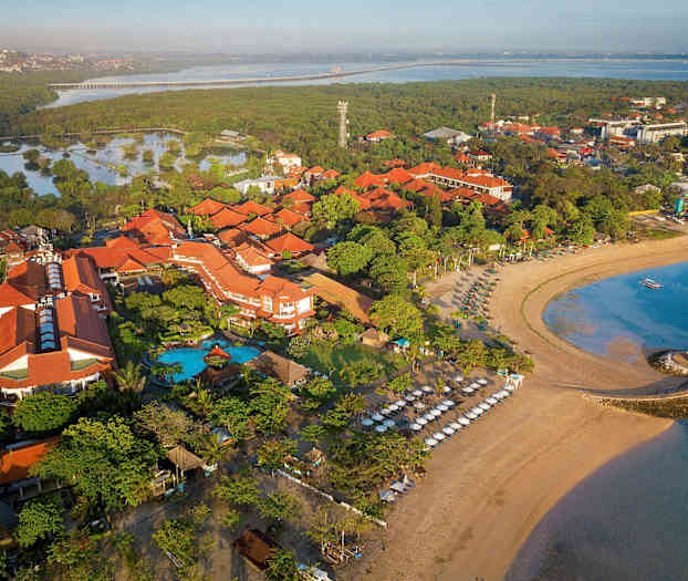 Luftfoto av et strandhotell omgitt av tropisk vegetasjon, stranden med solsenger og havet. (AI-generert tekst)