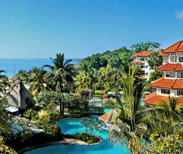 Bilde av et tropisk feriested med et basseng, palmer og bygninger med røde tak, beliggende nær sjøen. (AI-generert tekst)