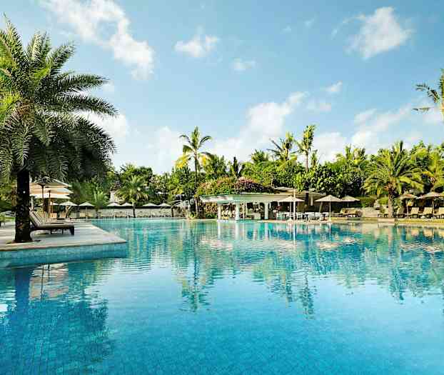 Et stort basseng omgitt av solsenger, parasoller og palmer, med en klar blå himmel i bakgrunnen. (AI-generert tekst)