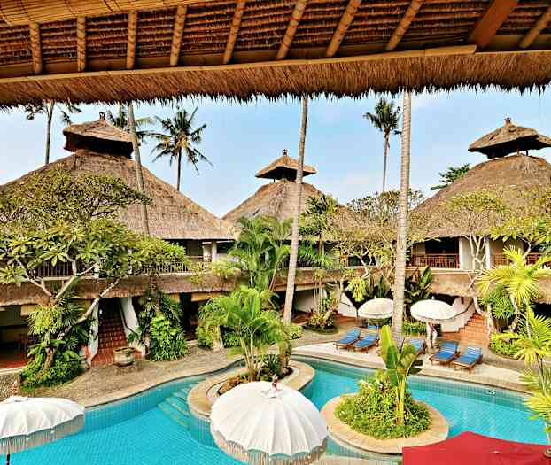 Et feriested med et basseng omgitt av palmer og bygninger med stråtak. (AI-generert tekst)
