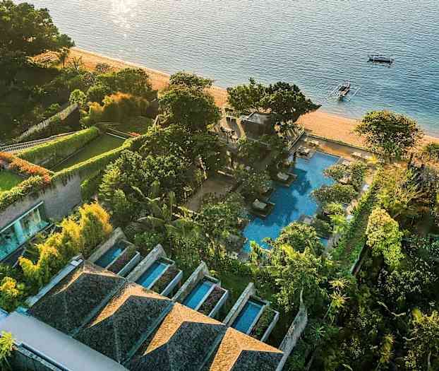 Et fugleperspektiv av et strandnært luksushotell med bassenger, grønne hager og stranden som grenser til havet. (AI-generert tekst)