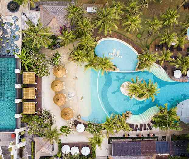 Luftfoto av et badeanlegg med solsenger, parasoller og frodig palmeselskaper. (AI-generert tekst)