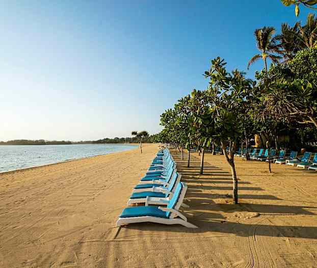 En sandstrand med solsenger og trær i bakgrunnen. (AI-generert tekst)