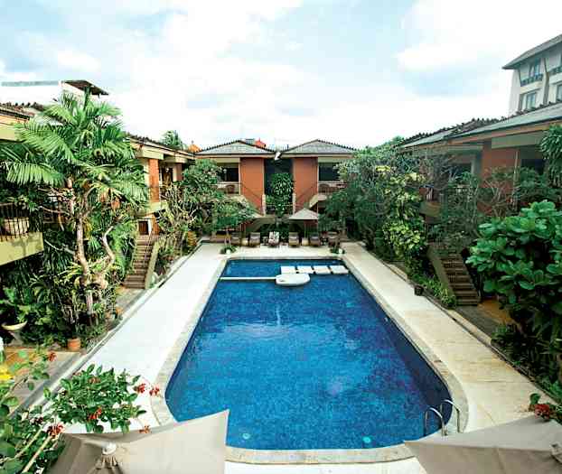 Bilde av et utendørs basseng med tropisk vegetasjon og omkringliggende bygninger. (AI-generert tekst)