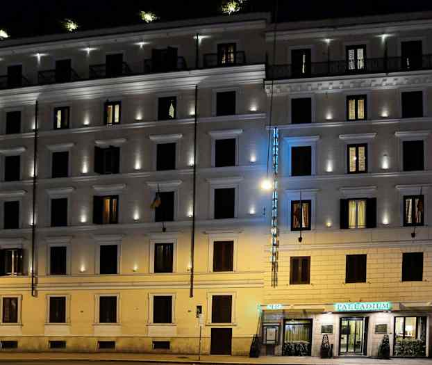 En flerbostadsbygning belyst om kvelden med et hotellskilt og opplyste vinduer. (AI-generert tekst)