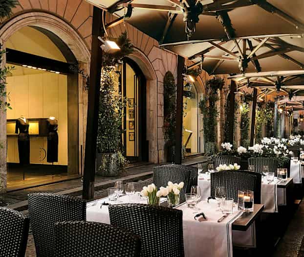 Uteservering med bord, hvite duker og blomsterdekorasjoner. (AI-generert tekst)