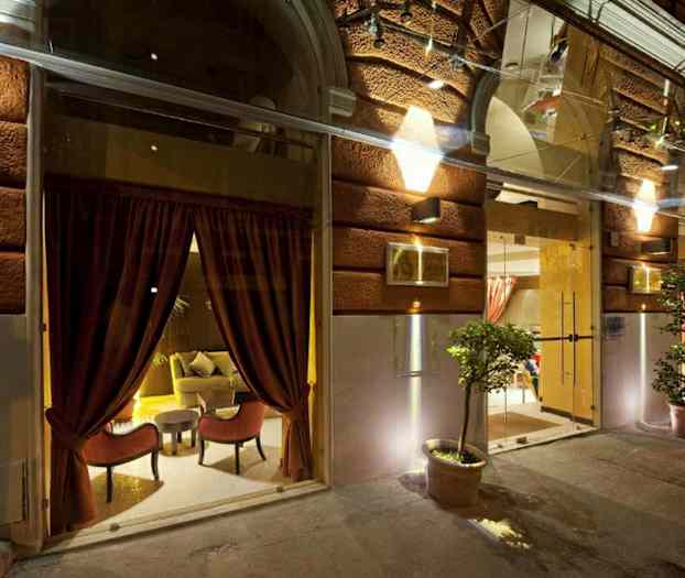 Bilde av inngangen til en bygning med opplyst fasade, store glassvinduer med røde gardiner og potteplanter. (AI-generert tekst)