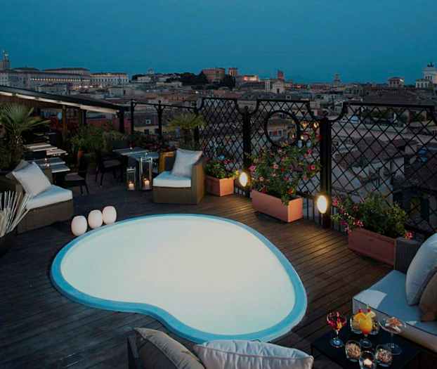 Bilde av en takterrasse med et lite basseng og sittemøbler, samt utsikt over en by i skumringen. (AI-generert tekst)