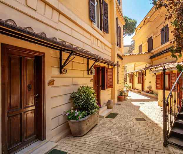 En solrik gårdsplass med jordgule bygninger, trapper og blomsterplantinger. (AI-generert tekst)