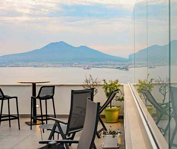 En terrasse med utsikt over havet og et fjell i bakgrunnen. (AI-generert tekst)