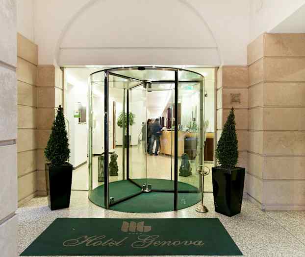 Inngangen til Hotel Genova med glassdører, grønn matte og to dekorerte planter. (AI-generert tekst)