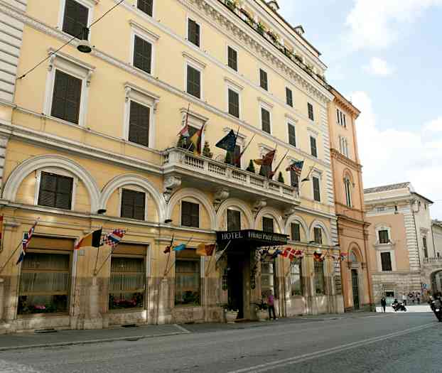En bygning med flere etasjer som har et hotelskilt og flagg fra forskjellige land. (AI-generert tekst)