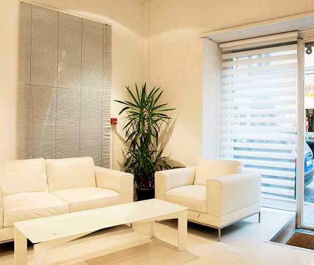 En lys stue med hvite møbler, en plante og store vinduer med persienner. (AI-generert tekst)