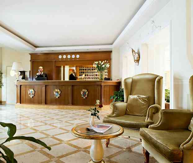 Et hotellresepsjonsområde med en resepsjonsdisk i tre og sitteplasser med grønne lenestoler. (AI-generert tekst)