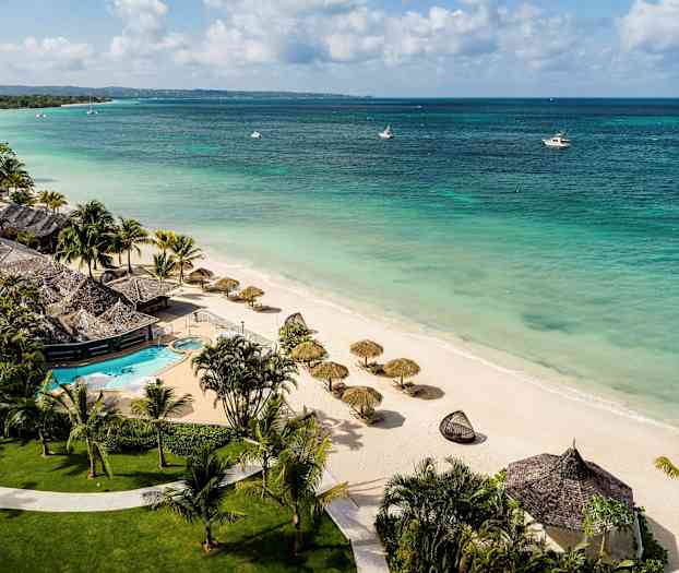 En strand med parasoller og et feriested med svømmebasseng. (AI-generert tekst)